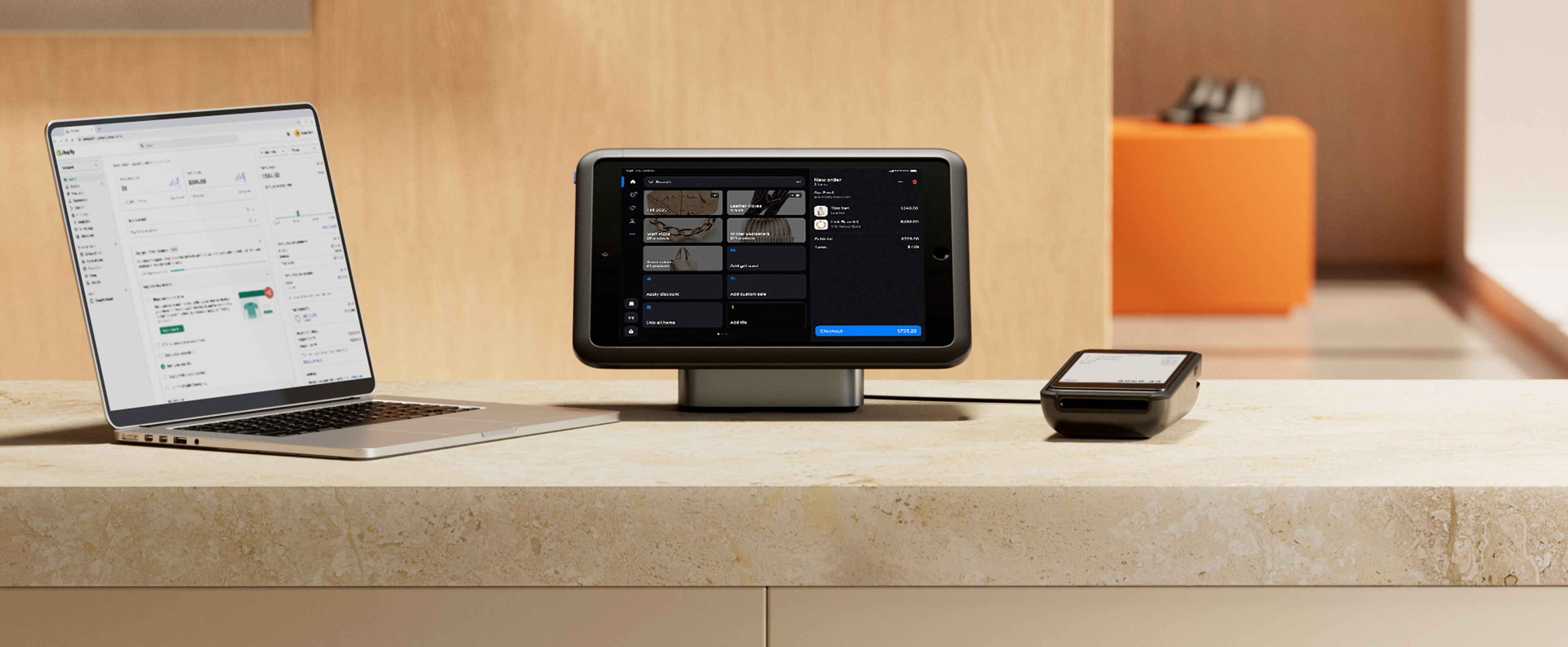 A retail store counter with a full set of devices. A laptop shows the Shopify back office, a tablet shows the Shopify POS app, and POS Terminal displays a checkout.