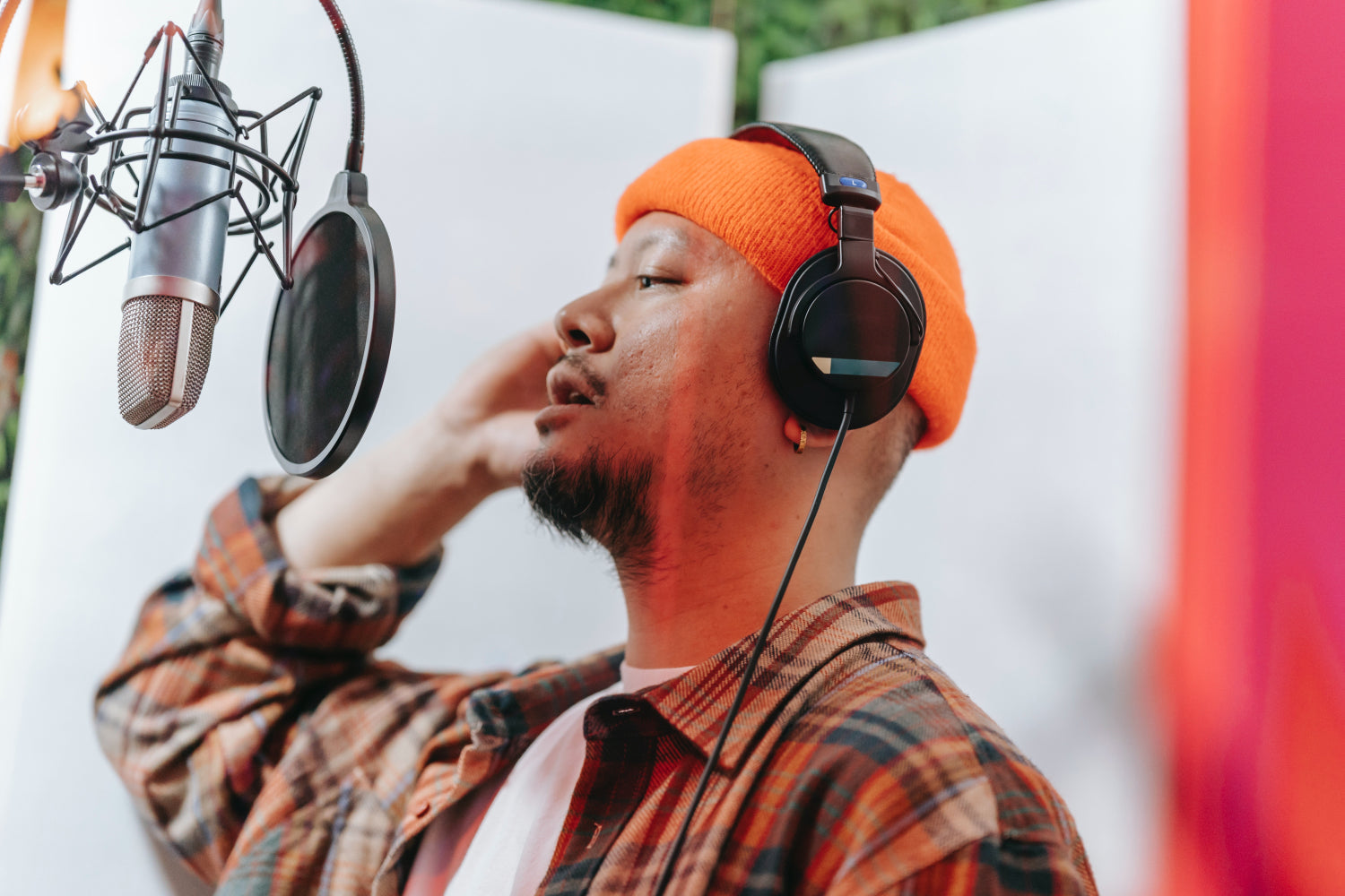 A person wearing an orange beanie and headphones sings into a professional microphone