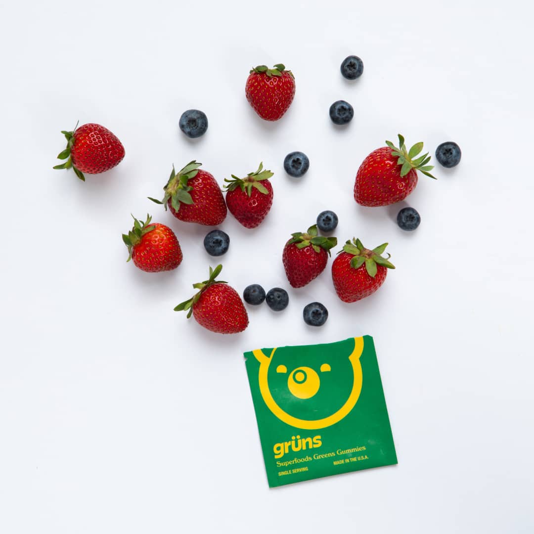 Strawberries and blueberries scattered around a packet of Grüns Superfoods Greens Gummies.