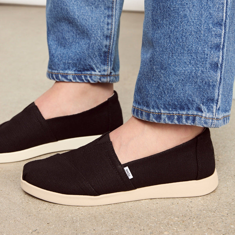 Up Close On Model Shot Of Alpargata Plus Slip On Casual Shoe In Black Canvas Styled With Denim Jeans Up Close On Model Shot Of Alpargata Plus Slip On Casual Shoe In Black Canvas Styled With Denim Jeans