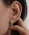 Close-up of a woman's ear wearing Lab Grown Sapphire Huggie earrings, featuring round white sapphires on 12mm hoops for everyday elegance.