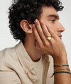 Man with curly hair holding his face, showcasing a Bar Cord Bracelet on his wrist. The bracelet stands out as a fashionable accessory.