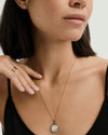 Woman wearing a Pearl Round Locket Necklace, showcasing a delicate gold chain with a round locket, complemented by close-up facial features.