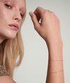 Woman wearing the Spheres Bracelet, a minimalistic gold accessory, with her hand on her wrist, emphasizing its elegant and versatile design.