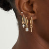 Close-up of a woman's ear wearing a Single Emerald Cut Gemstone Hoop Charm, showcasing a gold hoop with a dangling emerald-cut gemstone.