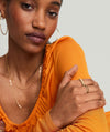 Woman wearing an orange top, showcasing the Charlotte Slim Ring in gold on her finger, complemented by matching gold necklace and earrings.