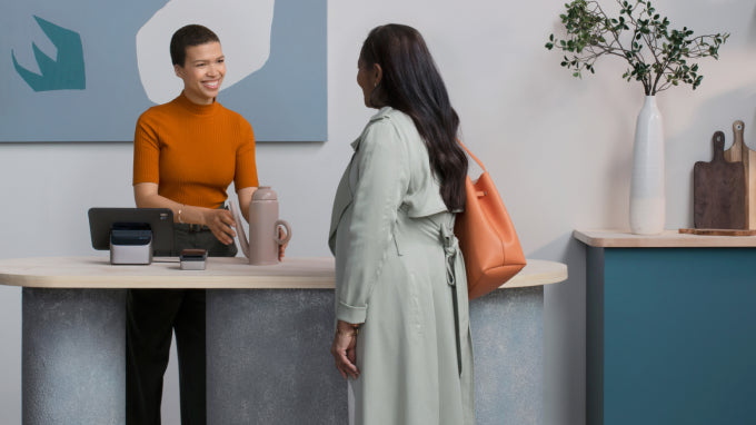 A sales associate helps with the sale of a tea pot for a customer using a POS tablet and card reader.